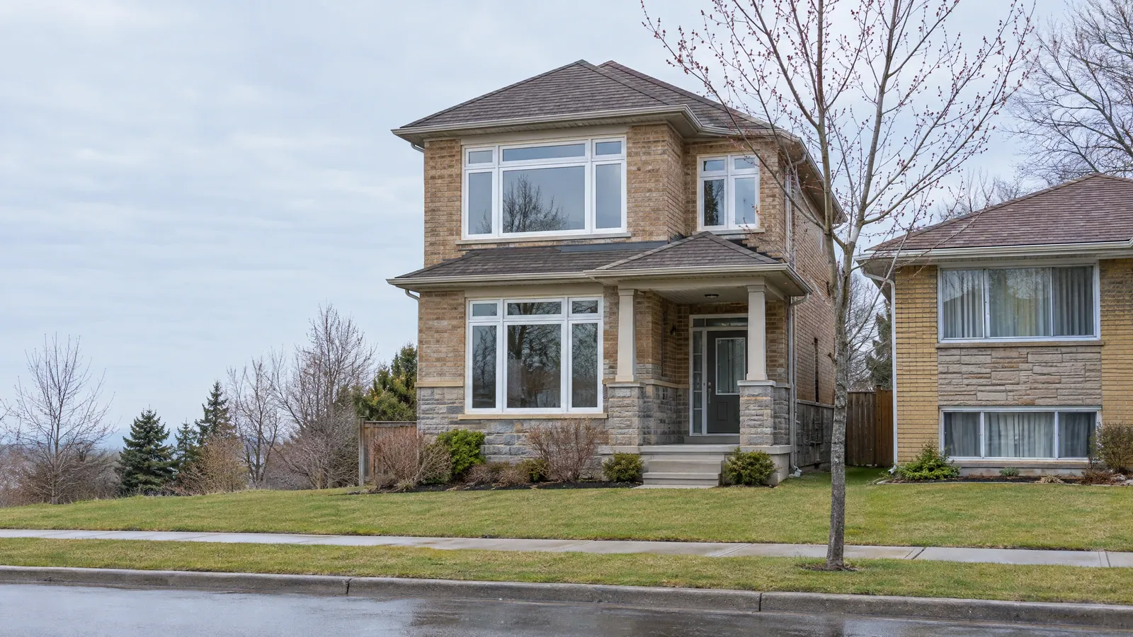 A late-2000s stone and brick home beside a 1980s side-split on an early-spring street