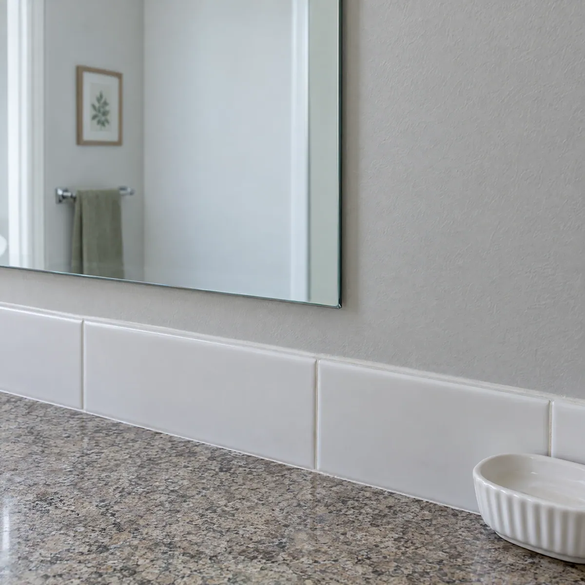 Close-up of a clear bathroom mirror edge above a white tile backsplash