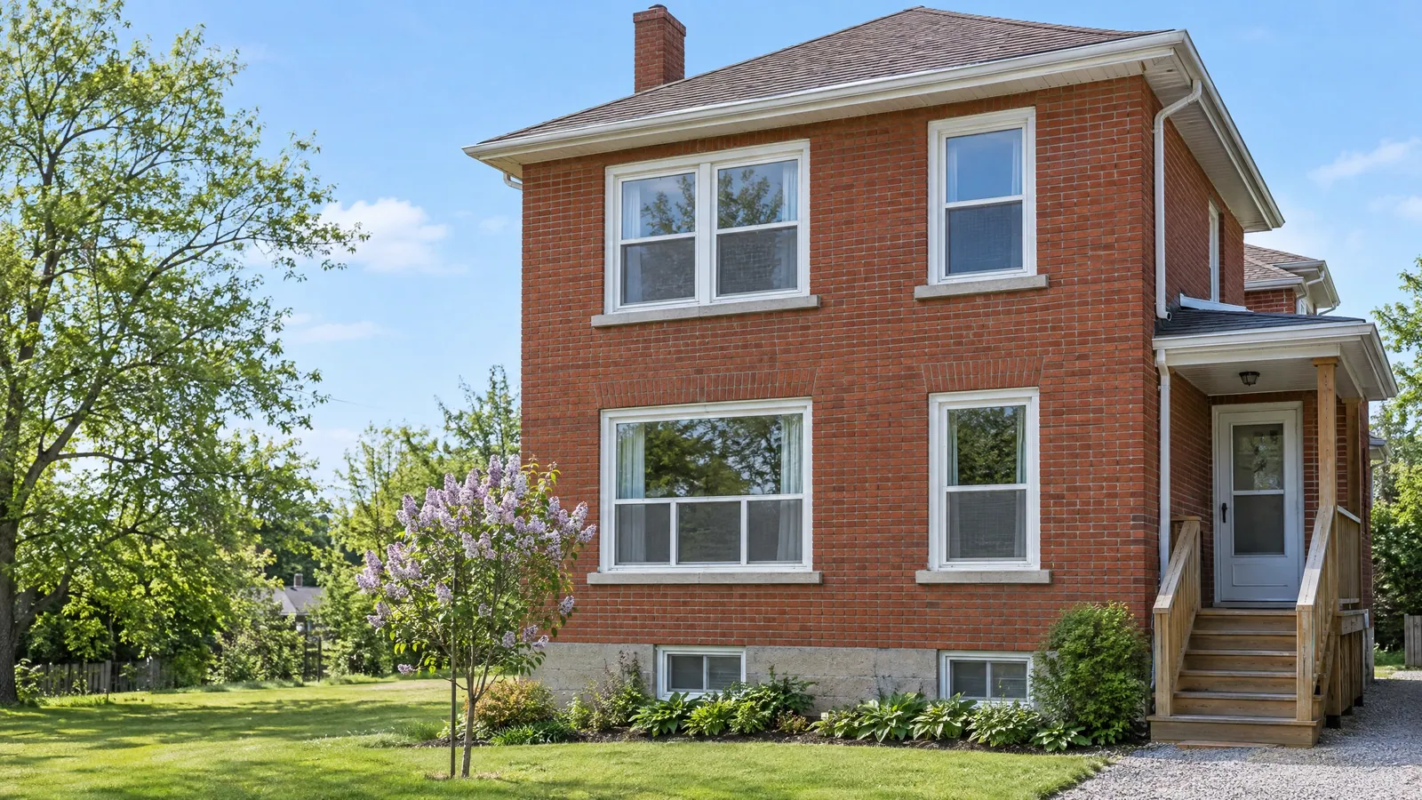 Two-storey red-brick house converted to a duplex, with white screened windows, two basement windows at ground level and a separate side entrance up wooden steps
