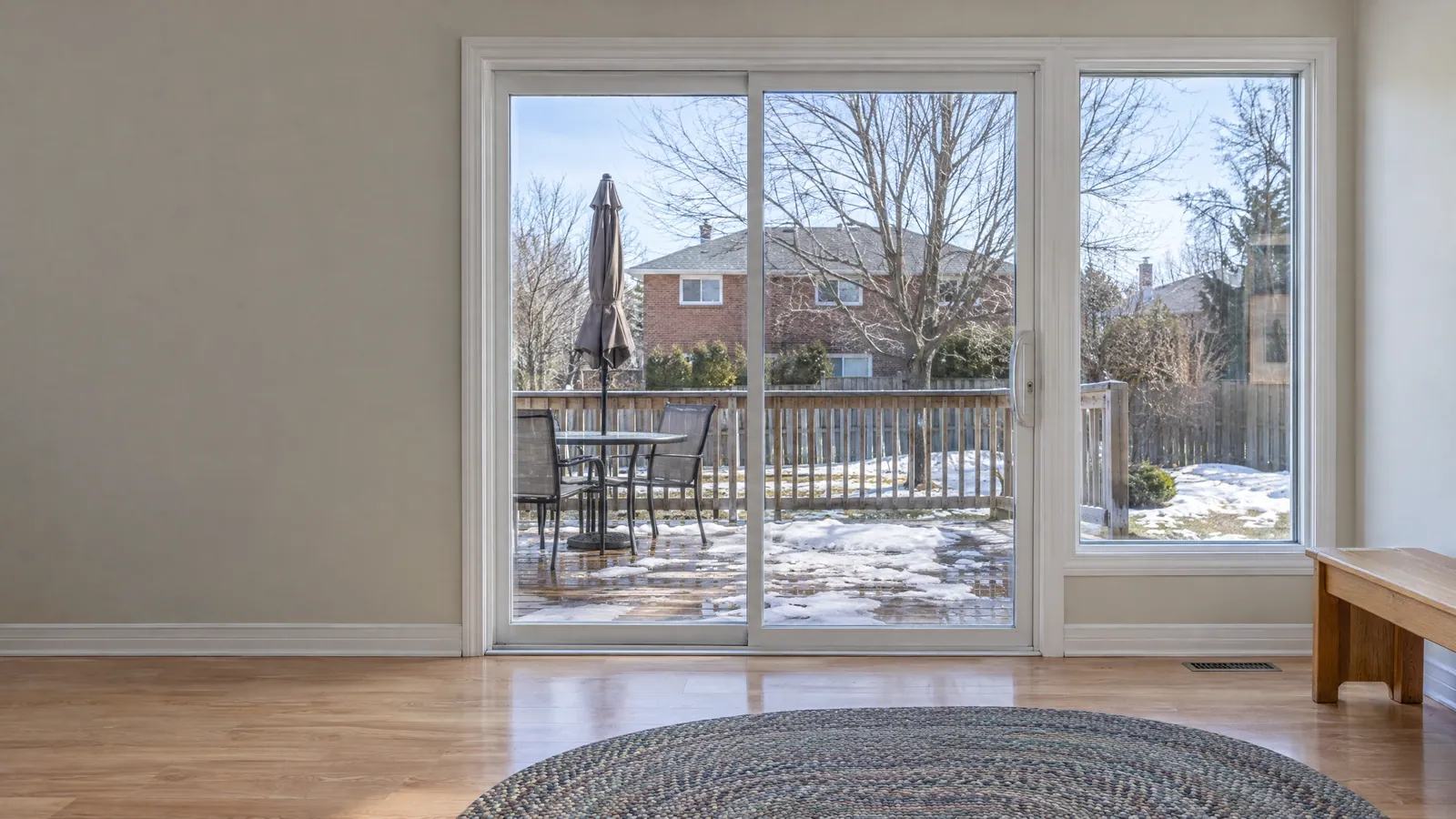 White vinyl sliding patio door in a family room, facing a slushy deck in early spring